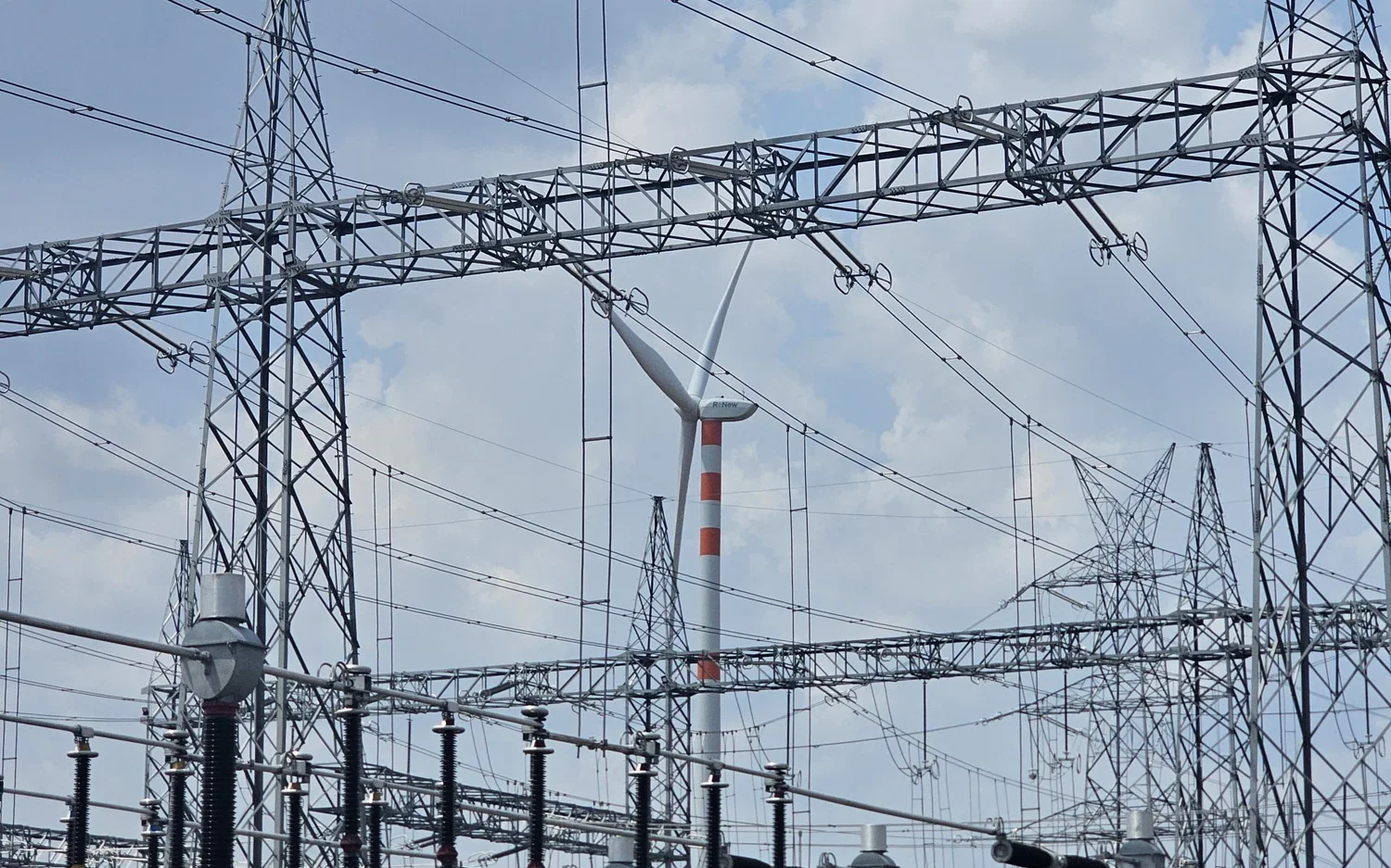 VEC substation under operation and maintenance — gantry structures, busbars and a wind turbine beyond